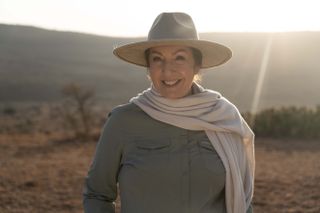 On Safari with Jane McDonald - Jane wearing safari clothes and hat, standing against a mountain background. 