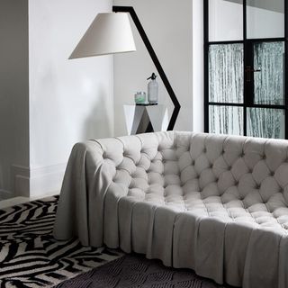 Grey buttoned sofa with a modern lamp and a rug