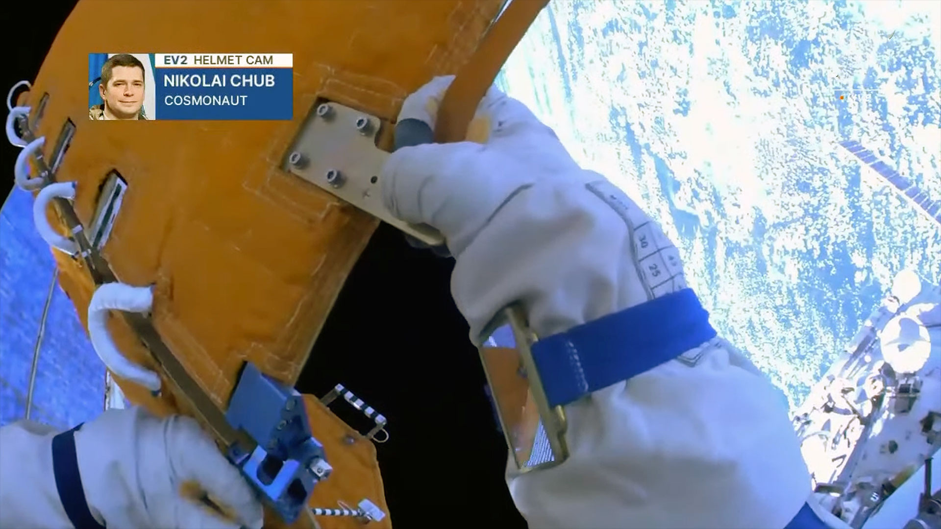 closeup of a cosmonaut's white glove holding an orange object during a spacewalk
