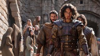 A group of soldiers descend a staircase while a group of villagers look on