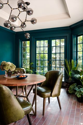 A turquoise blue dining room with green leather chairs and a statement silver light