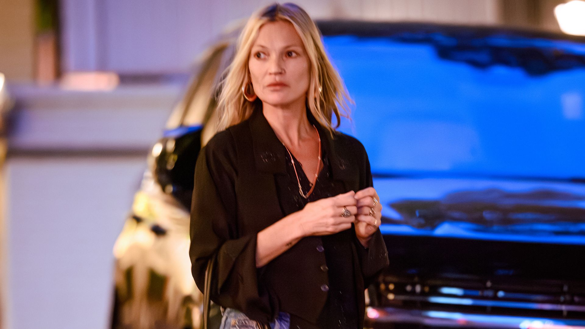 Kate Moss steps outside wearing stove pip jeans with heeled boots and a black blouse.