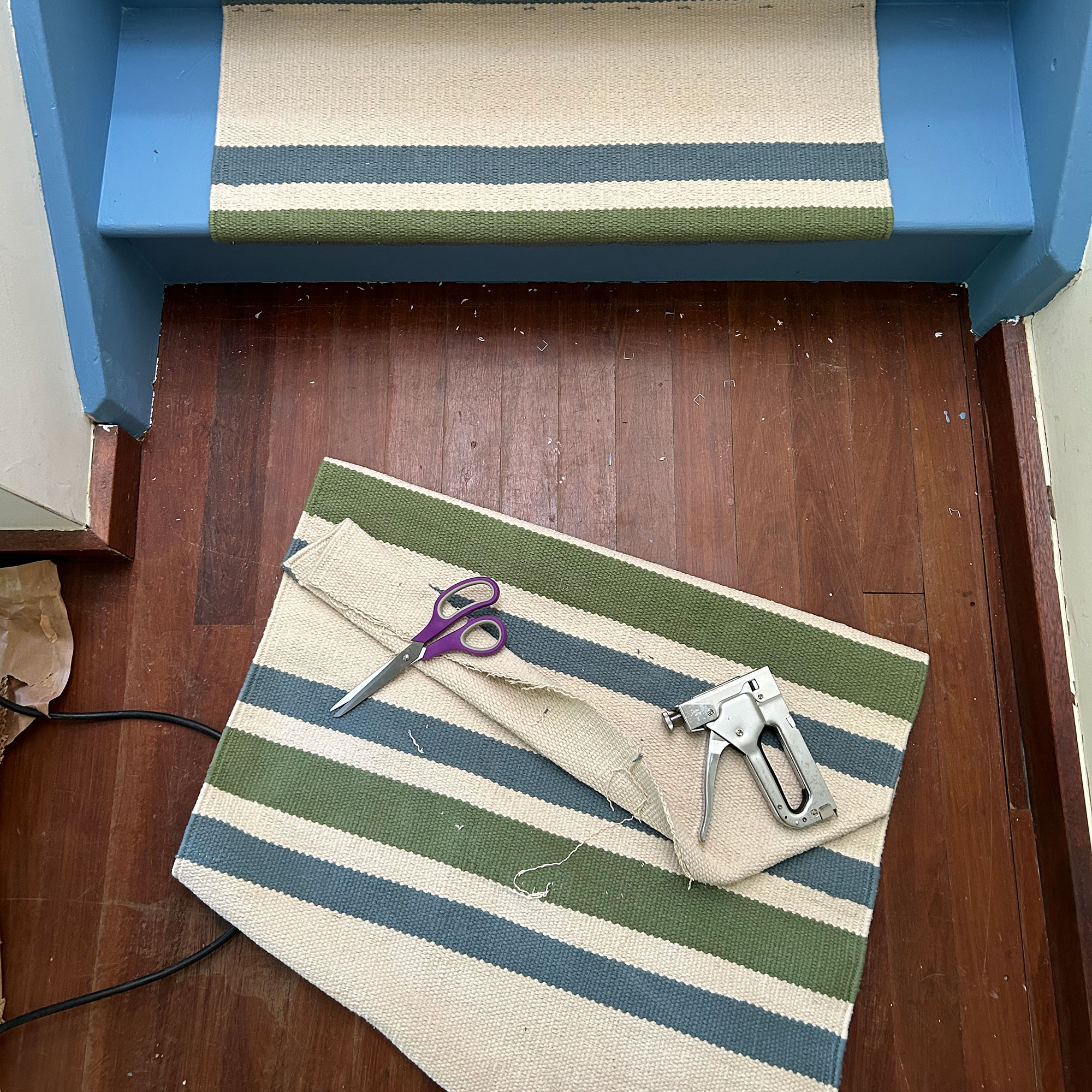 Scissors and staple gun sitting on striped fabric on wooden floor