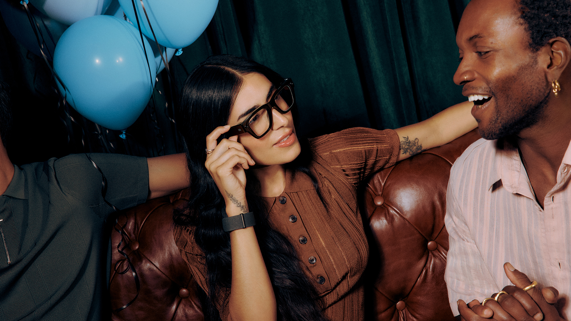 Meta Ray-Ban Display being worn by a woman sa on a sofa in between two people 