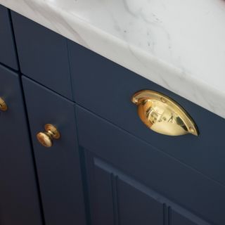 A close-up of a navy kitchen cupboard with a brass handle