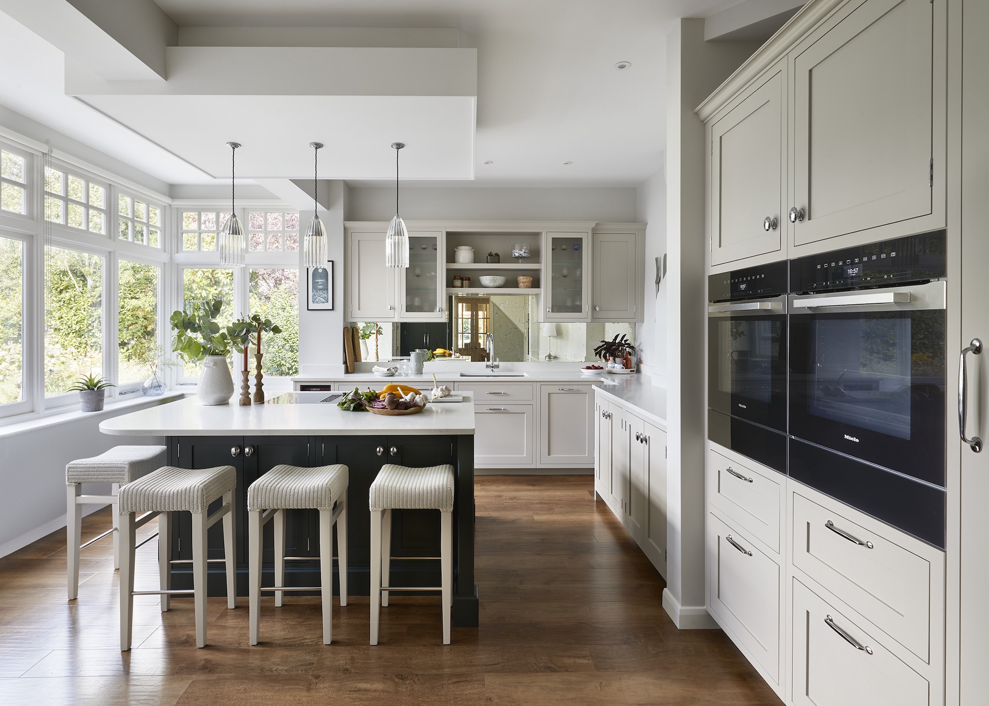 A kitchen with a small contrasting island in the middle. The island has storage and bar stools placed next to it. Above the island are three pendant lights hanging.