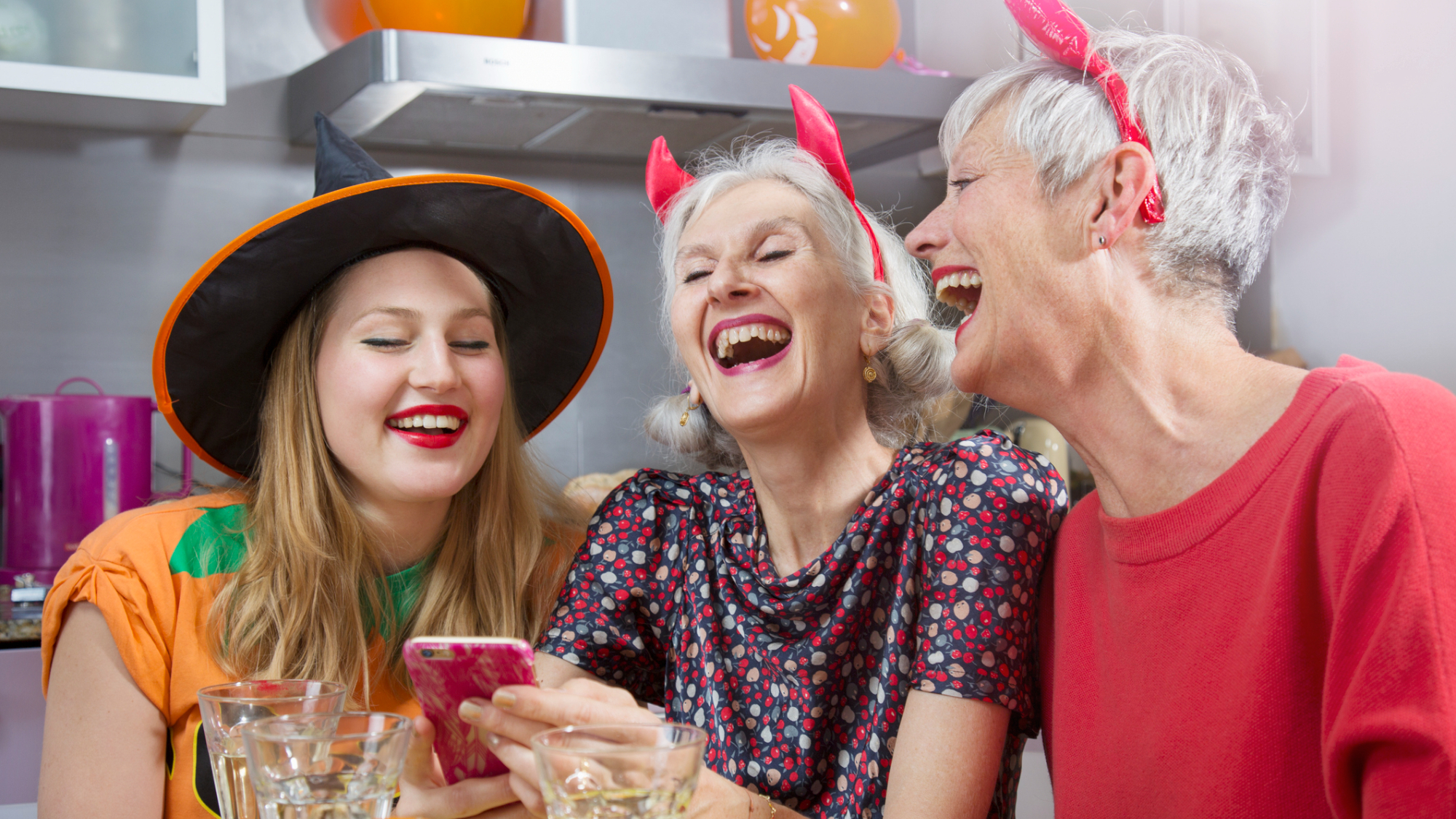 A group of women laughing, while dressed for Halloween, looking at a smartphone