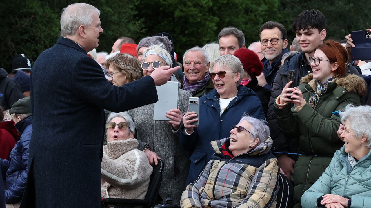 Prince Andrew wearing a long coat talking to a crowd of royal fans who are smiling and taking his photo on Christmas Day