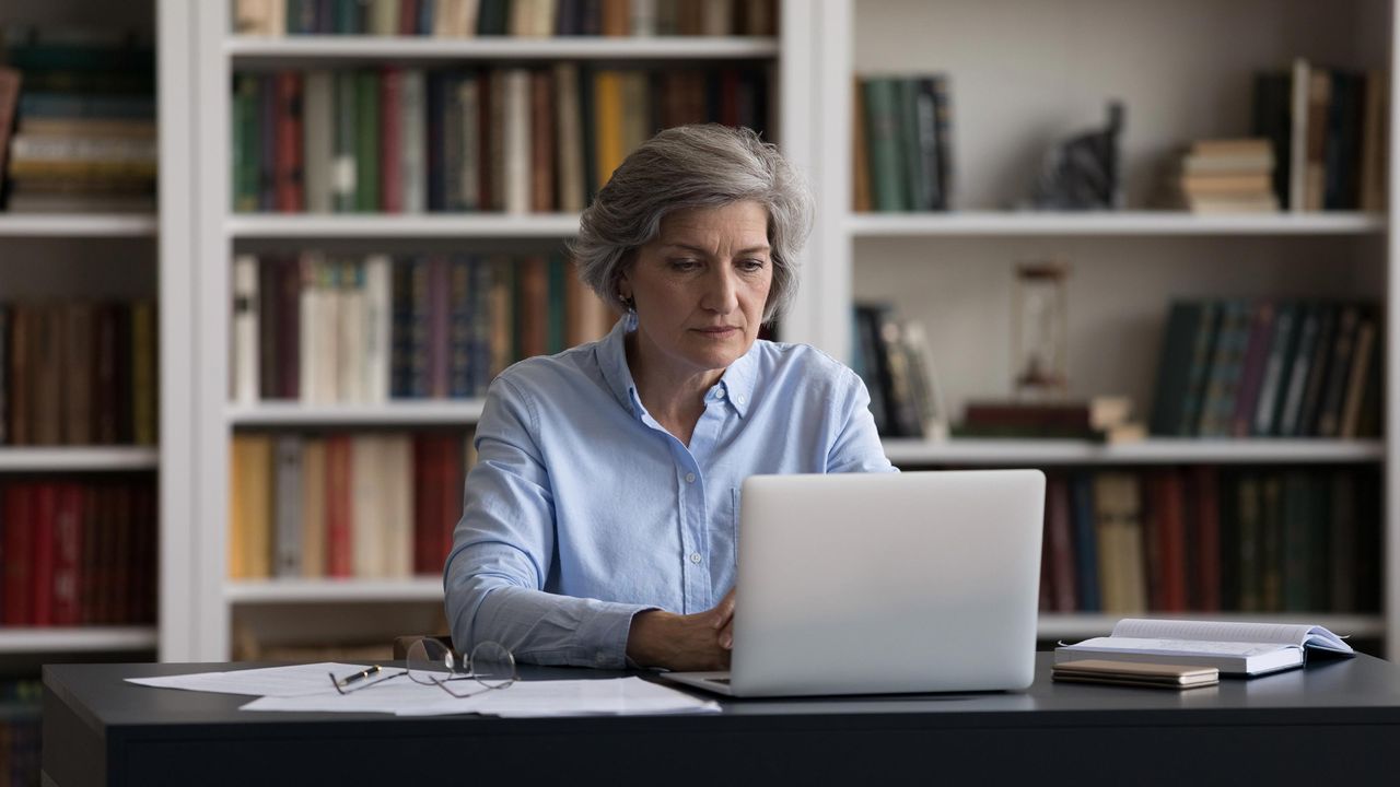 A woman in a home office looks at her laptop screen.