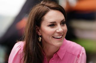 Kate Middleton wearing a pink dress and gold fern earrings and smiling