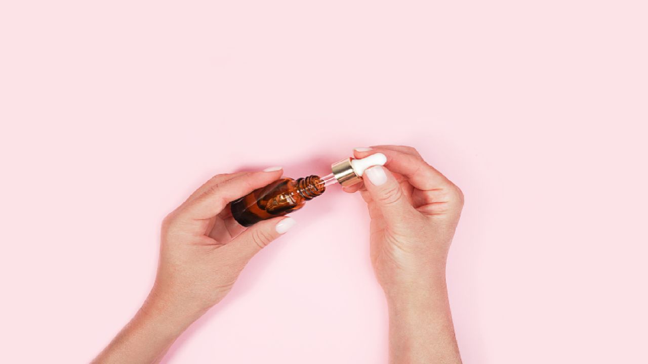 Hands holding beauty serum against pink background