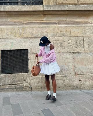 French woman wearing a pink cardigan and white skirt