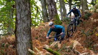 Two riders descending a wooded trail