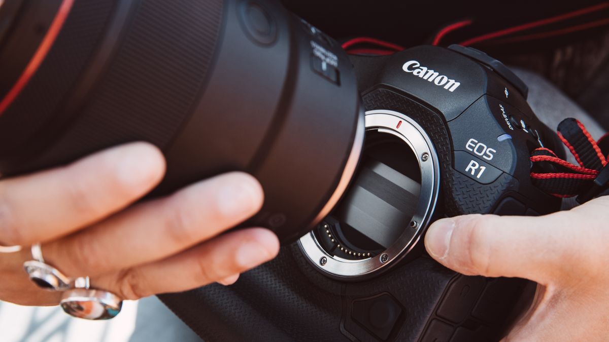 Canon EOS R1 camera held in a person&#039;s hands while they attach a lens