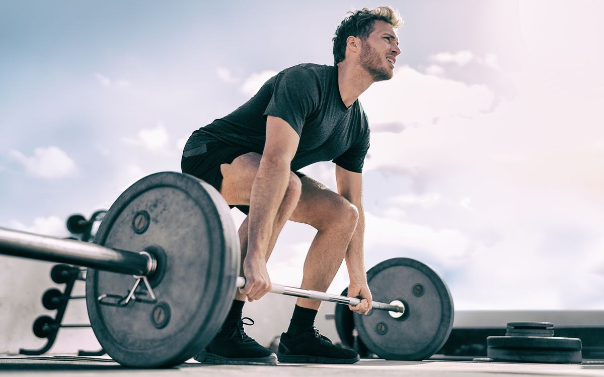 Man doing a barbell deadlift outdoors with a backdrop of the sky during workout