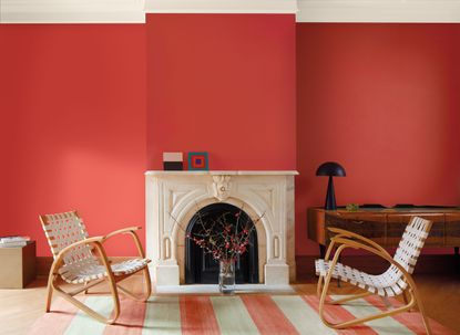 A living room painted in a rich pink color with a white fireplace and striped rug