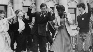 Prince Charles, the Prince of Wales learns a soul dance routine from 16-year-old Pearl Willie (on his left) and other members of St George's Secondary School in Maida Vale, London, 27th June 1978. The Prince is opening the Inner London Education Authority's Multi-Ethnic exhibition 'The Richer Heritage' at County Hall in London.