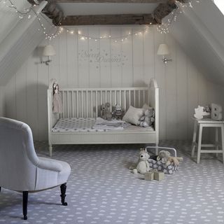 Grey nursery with patterned grey carpet and white cot bed and grey armchair