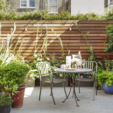 Garden patio with wood panelled walls and a small bistro set, surrounded by potted plants