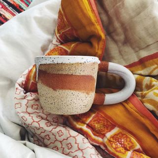 Artisan mug in earthy shades nested on terracotta colored quilts.