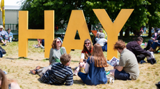 People sitting on the grass by a sign for Hay Festival