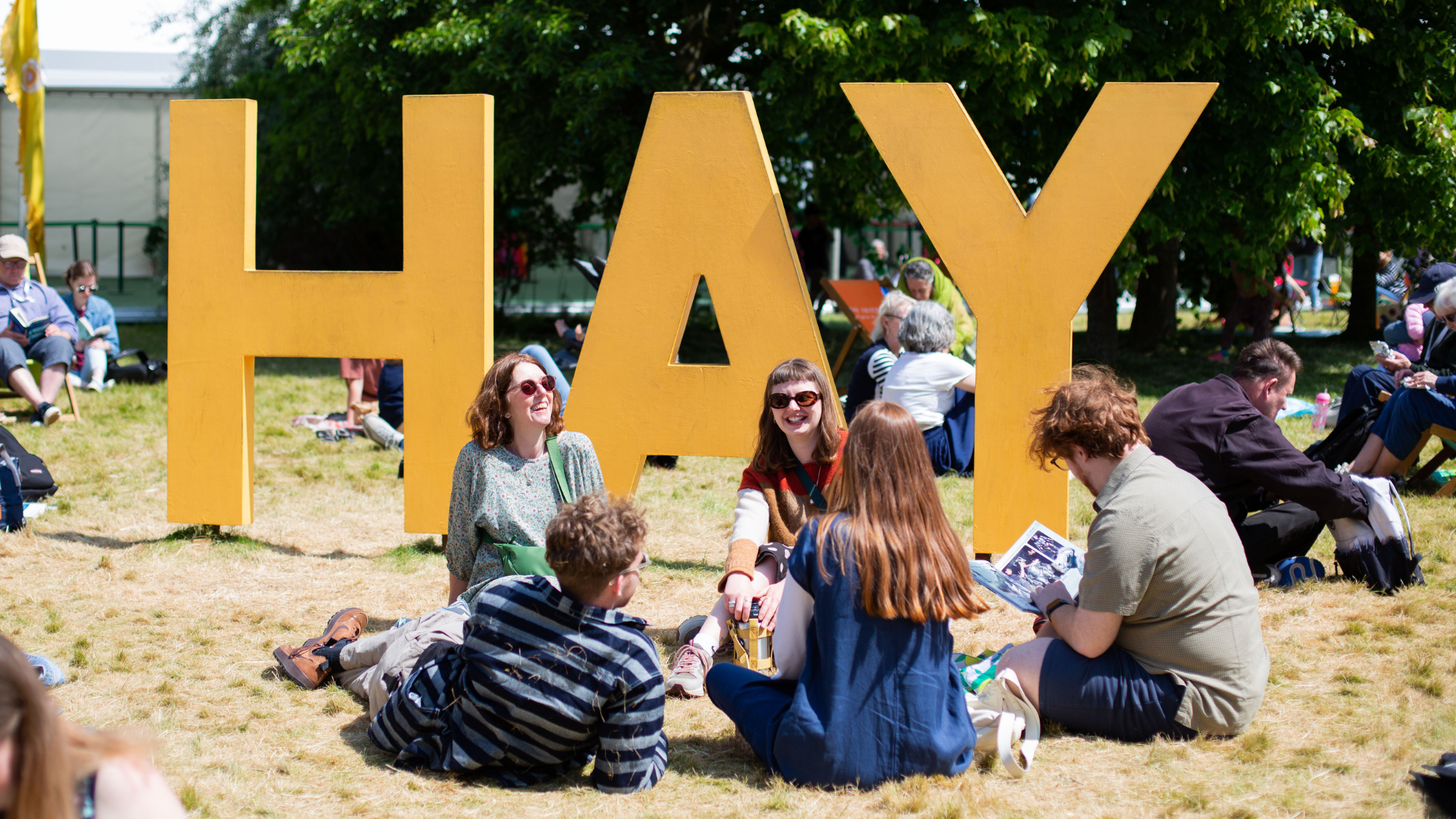 People sitting on the grass by a sign for Hay Festival