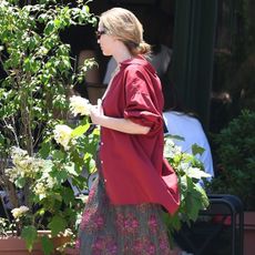 Jennifer Lawrence wearing a red button-down shirt, a floral pleated midi skirt, and sunglasses.
