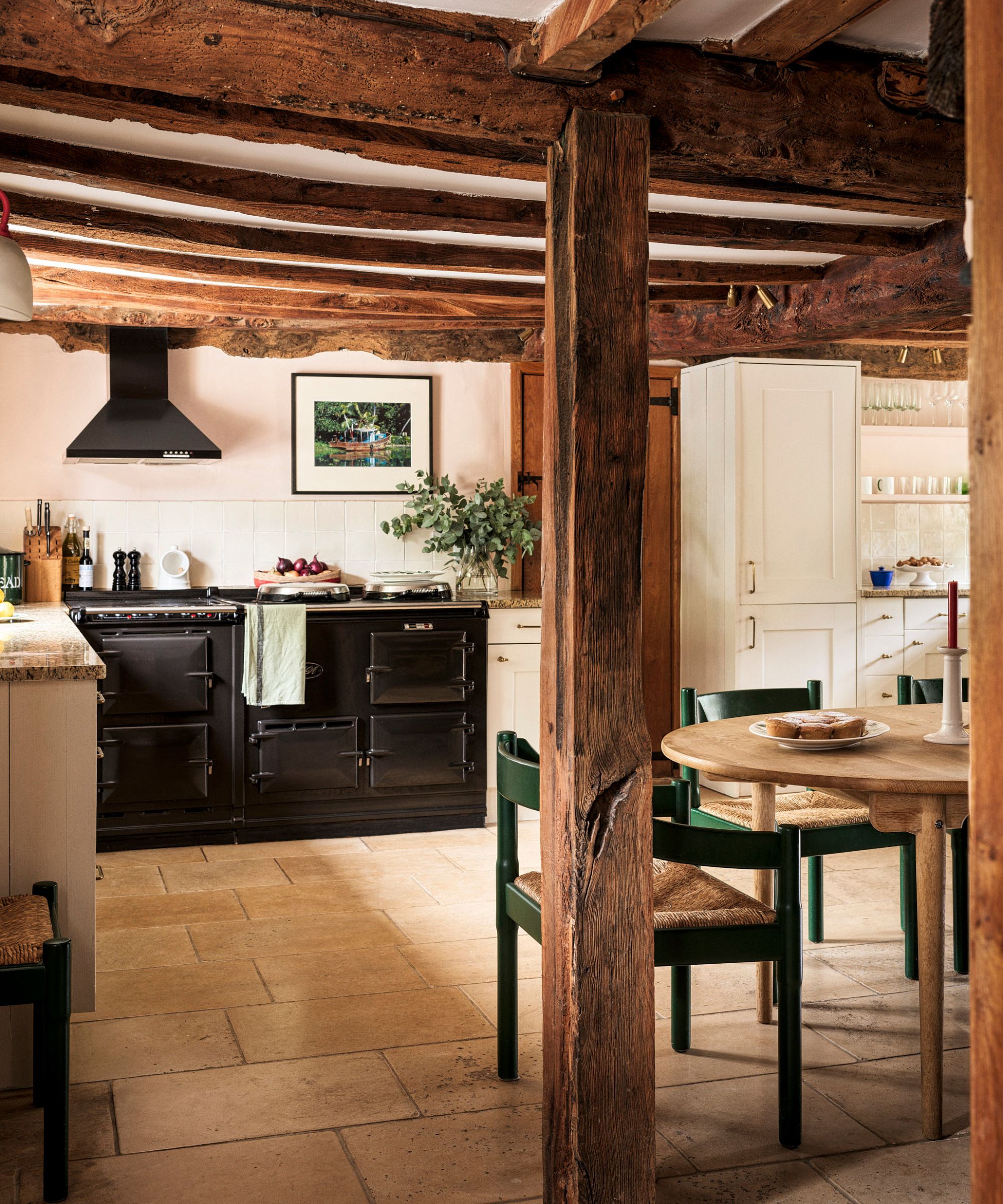 A cozy cottage kitchen with pink walls, white cabinets, and exposed wooden beams