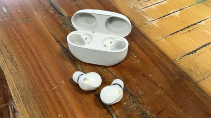 The Sony WF-1000XM5 wireless earbuds in white on textured wooden background