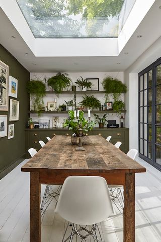 A wooden dining table with shelves in the background and lots of plants