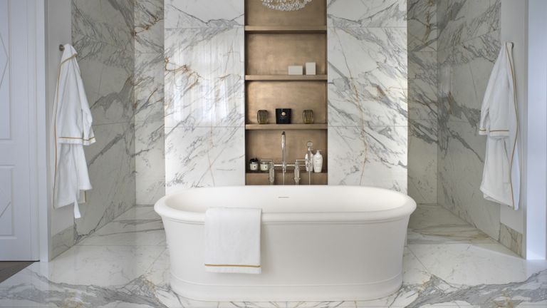 An example of bathroom layout ideas showing a marble bathroom with bronze built-in shelving and a white bath