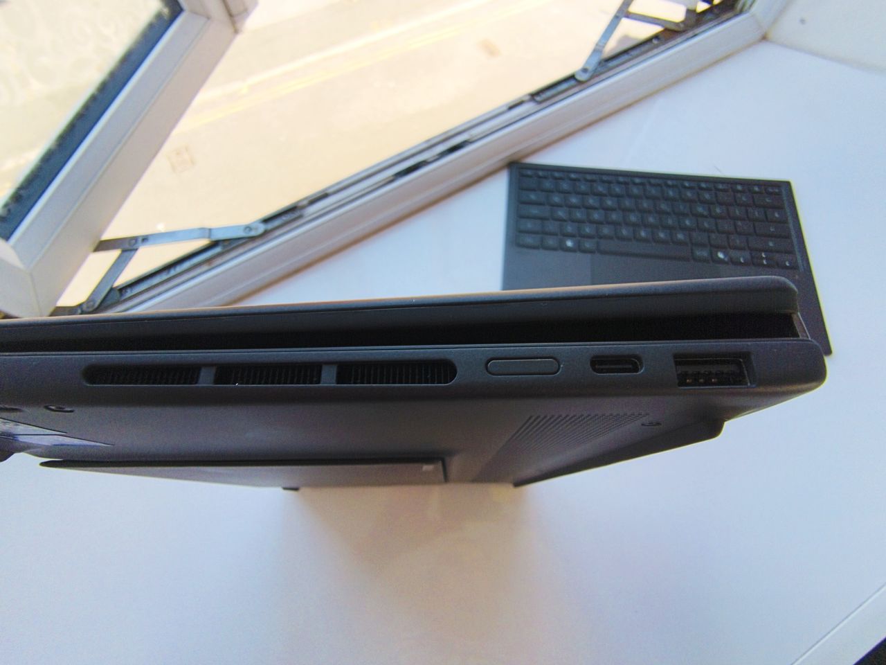 Side angle view of the ASUS Zenbook Duo in traditional laptop mode, displaying the Windows lock screen showing the time 15:52 against a mountain landscape background next to an open window.