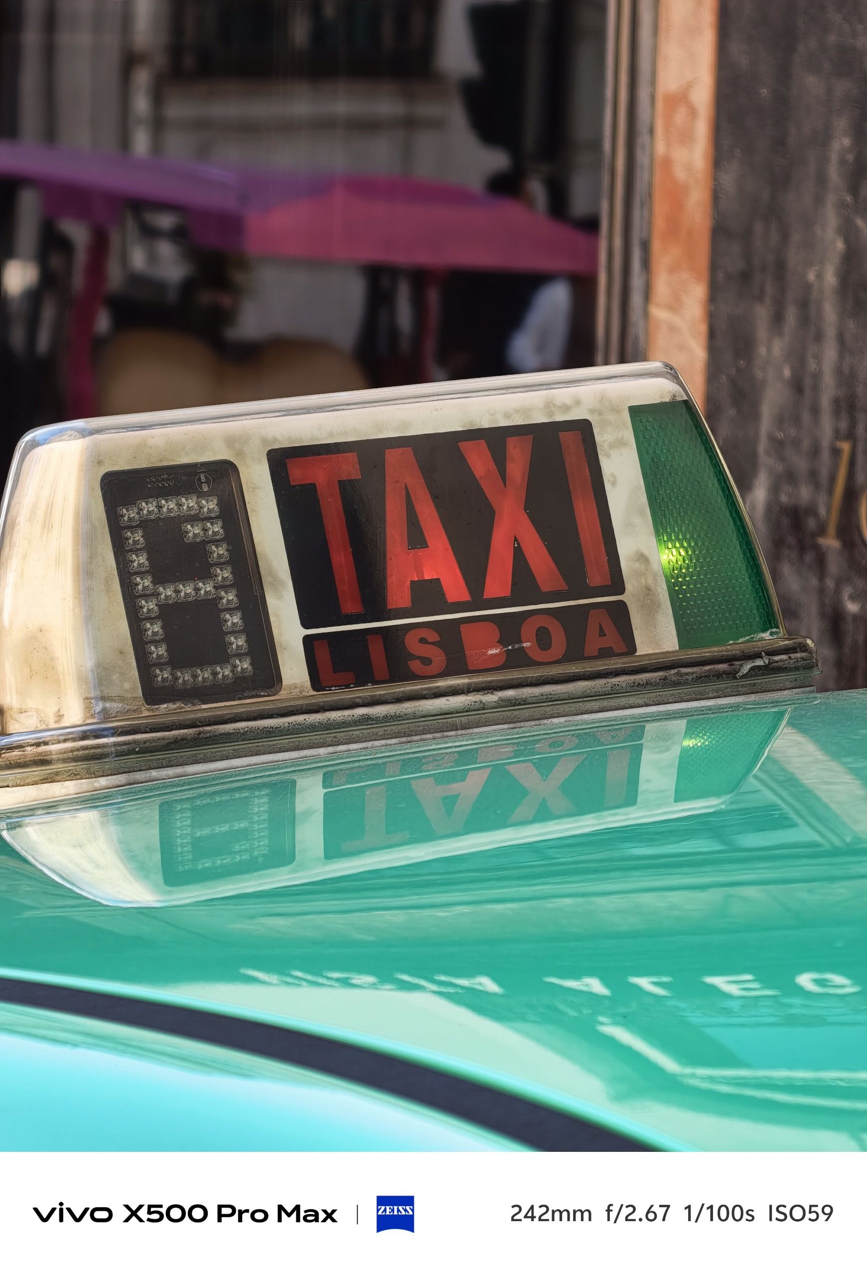 Close view of the roof sign on a turquoise Lisbon taxi, with an ornate building facade behind.