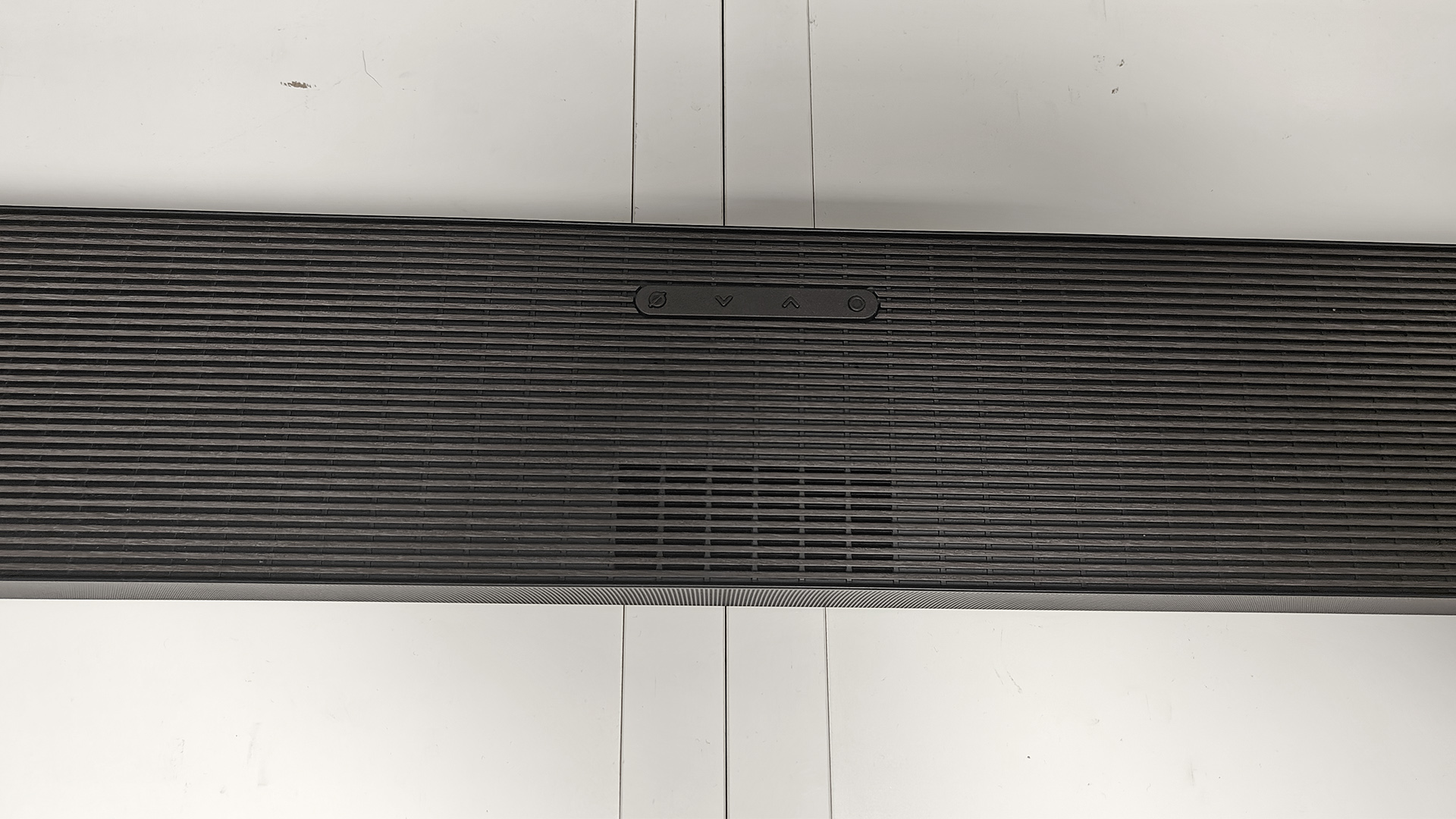 Samsung HW-QS90H Dolby Atmos soundbar on white shelving unit viewed from above and focuse on middle of soundbar
