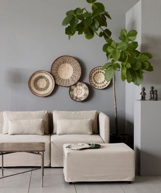 Mono natural wall plate decor display in gray living room, with neutral sofa, and tall potted tree.