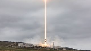 a timelapse exposure of a daytime rocket launch results in a bright beam of light climbing into the overcast sky
