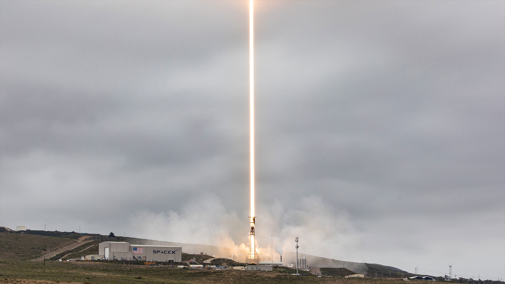 a timelapse exposure of a daytime rocket launch results in a bright beam of light climbing into the overcast sky