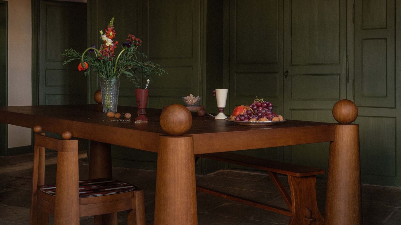 Close-up of flared-leg wood dining table against moss green panelled wall