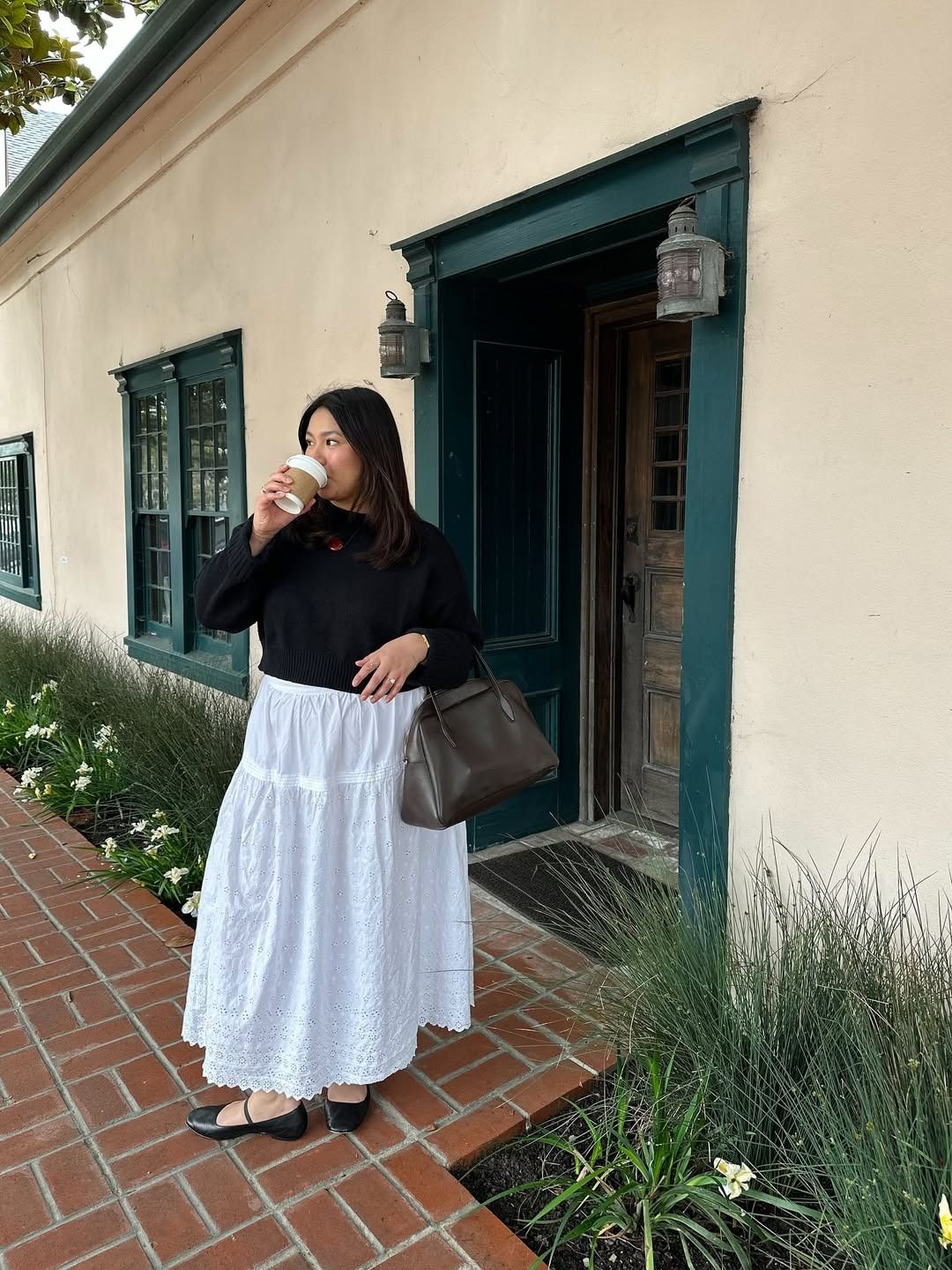 Influencer Marina wears a white midi skirt with ballet flats and a black chunky knit sweater.