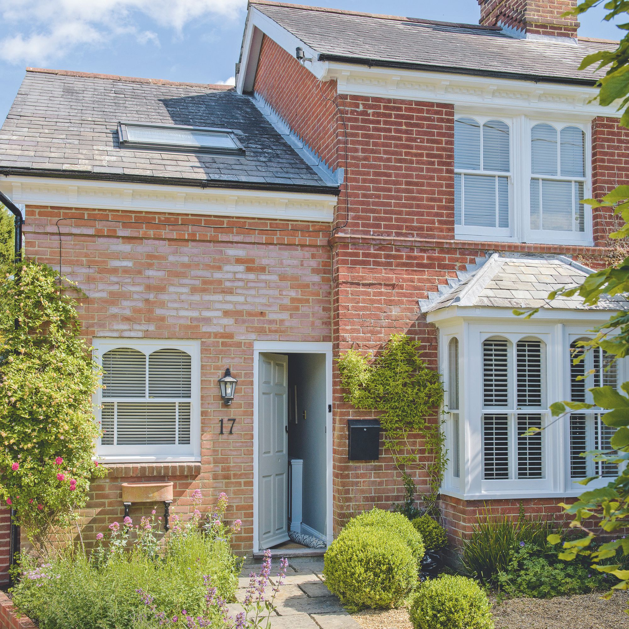 Exterior of a cottage with white windows and an open front door, with a pathway and gravel garden in front