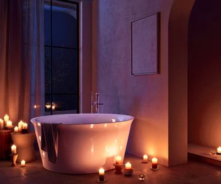 freestanding white bath in dark bathroom with lots of candles placed around