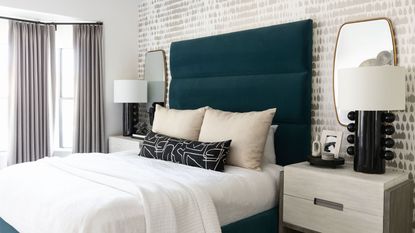 Modern bedroom setup with teal blue teal velvet headboard and mirrors above both bedside tables