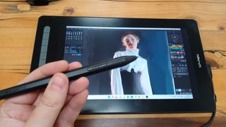 Best drawing tablets; a photo of a hand holding a stylus in front of the XP-Pen Artist 16 (2nd gen) drawing tablet.