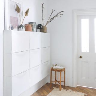 White front door in a white hallway with a shoe rack to the left