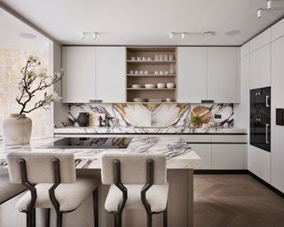 kitchen with marble worktops, streamlined taupe handless cabinets and drawers and island with cream barstools