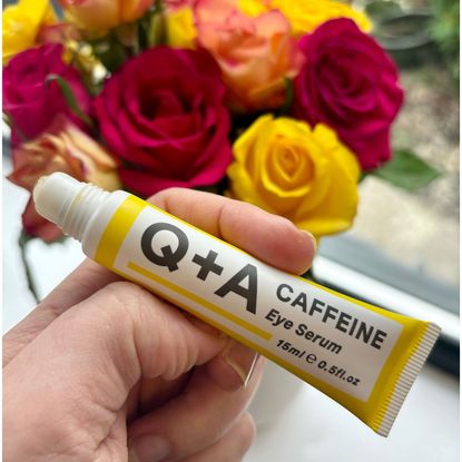 A shot of the Q+A eye serum being held in front of some flowers