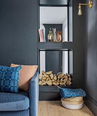 blue living room with blue sofa, fire wood stacked on shelf with books and whiskey on shelve above
