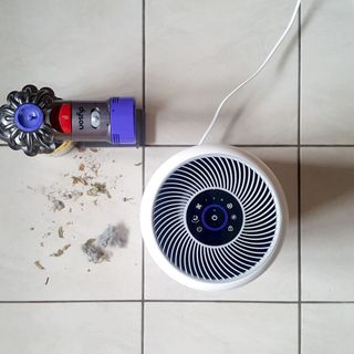 The Levoit Core 300S air purifier next to a Dyson vacuum cleaner with a pile of dust next to it