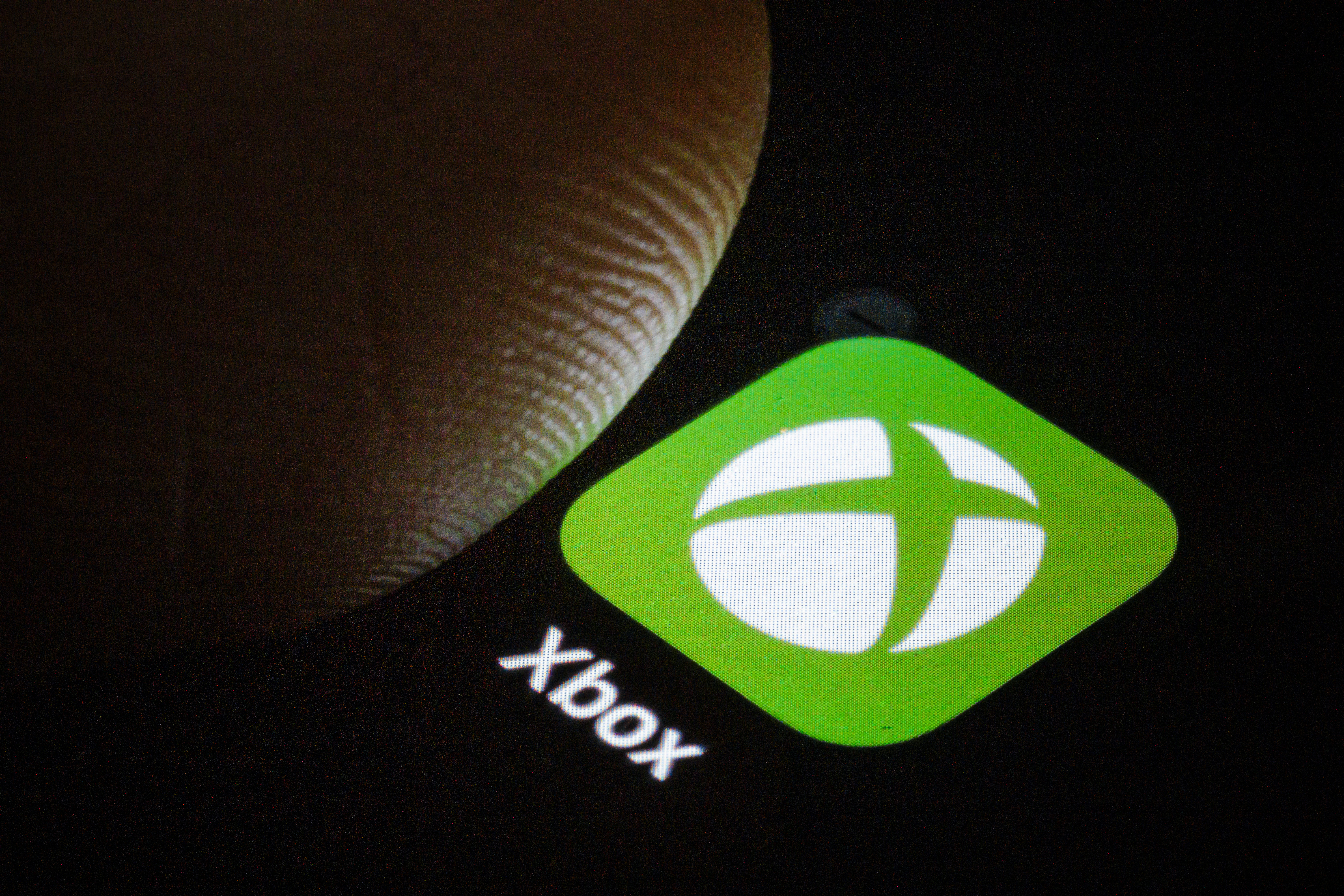Xbox logo on a smartphone screen with a thumb hovering over it