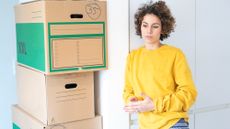 Contemplative woman standing next to a tower of moving home boxes